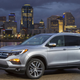A photo of a silver Honda Pilot crossover with a city skyline in the background.